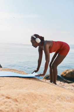 Kırmızı mayo giymiş odaklanmış bir kadın sakin denizin kenarındaki mavi yoga minderine uzanıyor ve huzurlu sabahın tadını çıkarıyor.