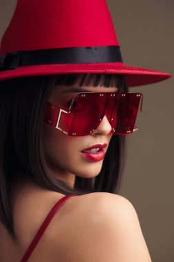 Kırmızı şapka, güneş gözlüğü ve kırmızı bir elbise. Yanları çivili kırmızı bir şapka takmış bir kadın. Güneş gözlüğü ve parlak kırmızı bir elbise takıyor.