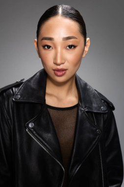 Asyalı kadın, siyah deri ceket, stüdyo resmi, gri arka plan. Tarz sahibi Asyalı bir kadın, siyah deri ceketli bir portre için tarafsız gri bir arkaplana poz veriyor..