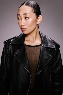 Siyah deri ceketli moda Asyalı kadın kameraya poz veriyor, yana bakıyor. Şık ve kendine güvenen kadın model şehir ortamında.