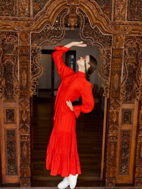Şık kırmızı elbiseli bayan zarif bir şekilde ahşap girişte duruyor..