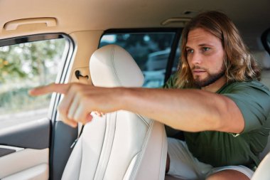 Uzun saçlı bir adam, bir aracın arka koltuğundan ileri doğru nişan ve niyet taşır.