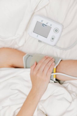 Kan basıncı monitörü ve kolunda kelepçeyle yatakta yatan bir kadın. Kan basıncını evde ölçüyor. sağlık hizmeti kavramı.
