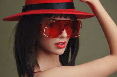 Kırmızı şapka, güneş gözlüğü, eli başının üstünde poz veren bir kadın, güneş gözlüğü, şık ve kendine güvenen, şık bir dış çekim, şık bir zarafet ve rahat bir ortam.