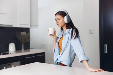 Modern mutfakta müzik ve kahveden hoşlanan, kulaklıklı ve elinde kahve tutan bir kadın.