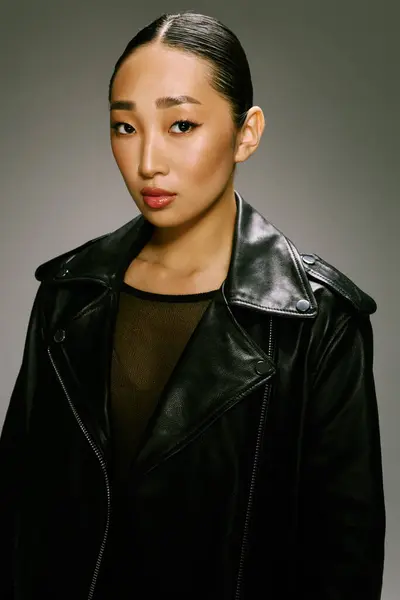 stock image Fashion asian woman wearing a black leather jacket posing in front of a gray background. portrait of stylish asian female model.