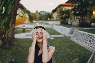 Parkta palmiye ağaçlarının önünde duran, elleri yüzü üstünde stresli bir kadın.