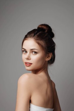 Beyaz elbiseli genç bir kadın gri arka planda kameraya poz veriyor..