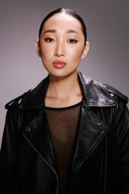 Moda, Asyalı kadın, siyah deri ceket, stüdyo resmi, gri arka plan. Siyah deri ceket giyen şık Asyalı bir kadının portresi. Stüdyo ortamında basit bir fotoğraf için poz veriyor.
