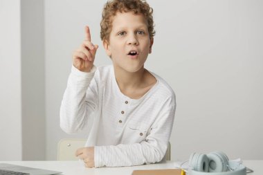 Evinde dizüstü bilgisayarla öğrenen güler yüzlü beyaz bir çocuk, rahat evinde, modern bir masada oturuyor. Elning ve online eğitime dalmış, yüzünde mutlu bir ifadeyle,