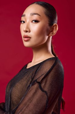 Saf siyah bluzlu Asyalı kadın kırmızı arka planda poz veriyor. Kolları çapraz ve elleri kalçasında. moda Asya tarzı.