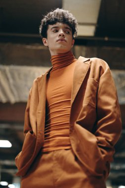 Turuncu kıyafetli bir gencin modern moda portresi cesur bir şehir ortamında kendinden emin duruyor.