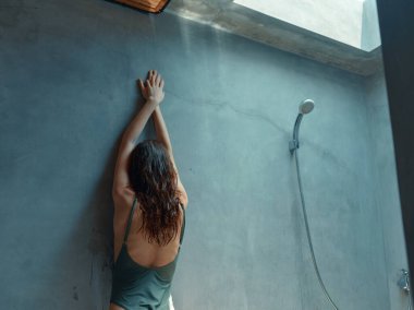 Mayolu bir kadın duşta, elleri duvarda, huzurlu ve rahatlatıcı bir anın tadını çıkarıyor..