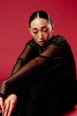 Siyah gömlekli ve taytlı, dizlerinin üstünde oturan Asyalı bir kadın..