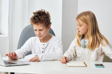 Evlerinde dizüstü bilgisayarları, kulaklıkları ve tabletleriyle ders çalışan mutlu Kafkasyalı erkek ve kız evlerinde rahat oturma odalarında bir masada oturuyorlar.