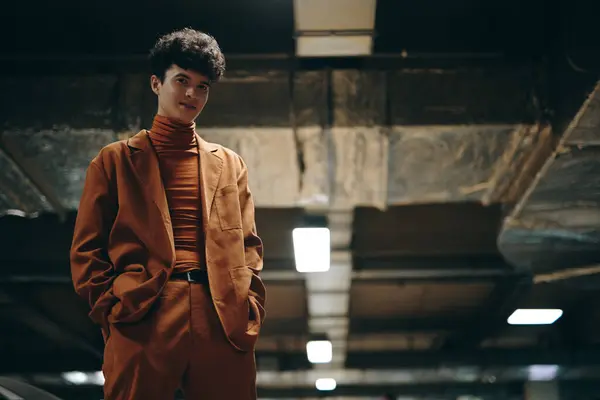 stock image A young man wearing a brown suit and turtleneck poses in a modern, stylish way in a parking structure