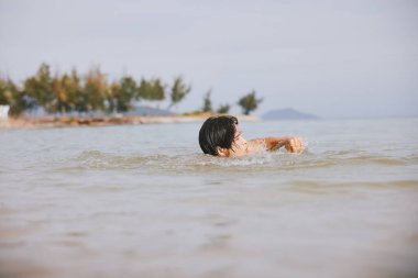 Tropikal Mavi Sularda Yüzen Neşeli Asyalı Adam: Aktif Tatil Eğlencesi ve Rahatlama