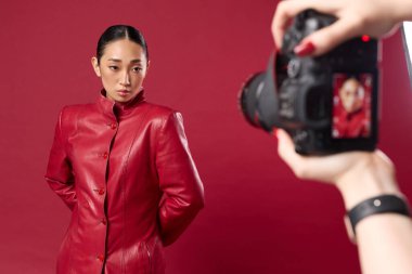 Modaya uygun Asyalı esmer, kırmızı arka planda kırmızı deri ceketli başka bir Asyalı esmerin fotoğrafını çekiyor..