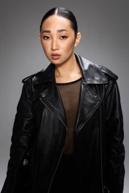 Siyah deri ceketli moda Asyalı kadın. Stüdyoda elleri kalçalarında poz veriyor..