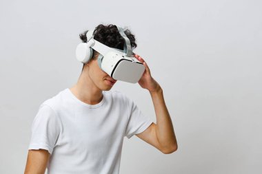 Genç bir adam, parlak bir VR kulaklık takarken sanal gerçeklik deneyimine dalmış, arka plan sade ve hafiftir, teknolojiyi ve kullanıcının dijital dünyayla olan ilişkisini vurgular.