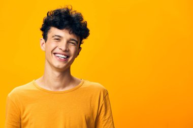 Kıvırcık saçlı, neşeli sarı arka planda gülümseyen mutlu genç adam, neşe ve pozitiflik taşıyor, reklamcılık, yaşam tarzı veya neşeli temalar için ideal.