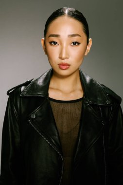 Asyalı kadın siyah deri ceket stüdyo resmi gri arka plan. Tarz sahibi ve modaya uygun Asyalı bir kadın, tarafsız gri arka planı olan bir stüdyo fotoğrafçısı için siyah deri bir ceket giyiyor.