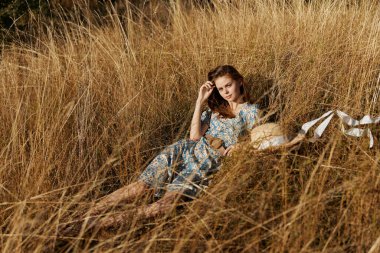 Mavi elbiseli kadın uzun çimenlerde dinleniyor. Şapkası sakin. Seyahat ve eğlence için güzellik anlayışı var.