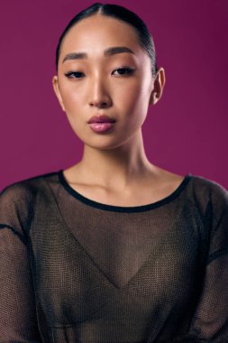 Kolları çapraz ve elleri kalçasında mor arka planda poz veren katıksız Asyalı bir kadın. Şık ve şık görünüm..