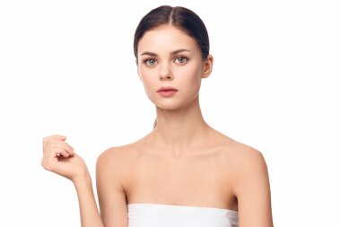 Beyaz havlu giymiş bir kadın yüzüne dokunuyor ve kameraya bakıyor. beyaz arkaplanda izole.