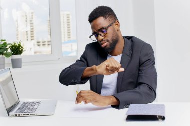 Kendine güvenen Afro-Amerikan iş adamı çağdaş ofis ortamında parlak bir masada dizüstü bilgisayar üzerinde çalışıyor..