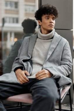 Gri ceketli, kaplumbağa yakalı, kot pantolonlu ve spor ayakkabılı şık bir genç..