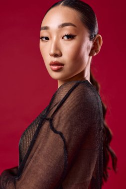 Siyah bluz giyen Asyalı kadın kırmızı arka planda poz veriyor gözleri kapalı ve elleri kalçasında. moda fotoğrafı.