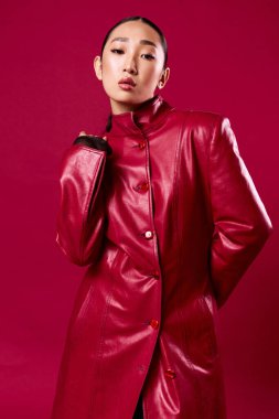 Esmer, şık kırmızı deri ceketli, kırmızı arka planda poz veren Asyalı bir kadın. Moda fotoğrafı..