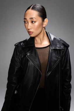 Siyah deri ceketli, taytlı, kameraya poz veren Asyalı bir kadın..
