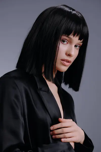 stock image Black suit, woman, black bob wig, gray background a woman in a black suit with a stylish black bob wig poses confidently with her hands on her hips against a minimalist gray backdrop