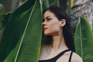 Siyah elbiseli kadın, doğada yeşil yapraklı ağacın yanında duruyor.