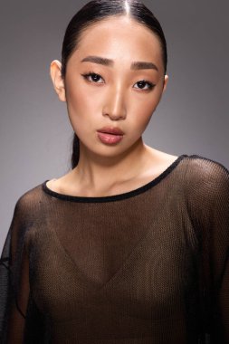 Gri arkaplan önünde fotoğraf çekimi için poz veren katıksız bluzlu moda Asyalı kadın. Genç Asyalı kadın şık ve kendinden emin görünüyor..