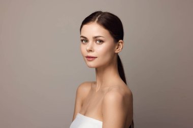 Beyaz elbiseli genç kadın gri arka planda kameraya poz veriyor. Reklam ve pazarlama amaçlı güzel ve şık bir imaj. Ticari kullanım için fotoğraf lisansı.