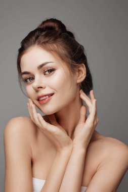 Elleri yüzünde poz veren genç bir kadın. Gri arka planda yakın çekim..