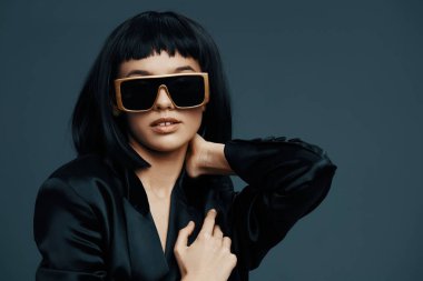 Kadın, siyah saçlı, güneş gözlüklü ve siyah ceketli.