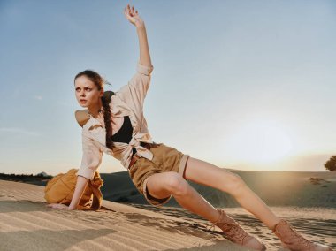 Güneşli bir günde kumlu kumulda uzanmış, elleri havada, mavi gökyüzünün altında uzanmış bir kadın.