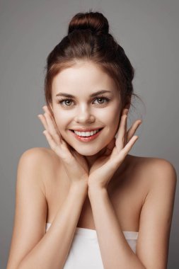 Elleri yüzün üzerinde poz veren genç bir kadın kameraya bakıyor..