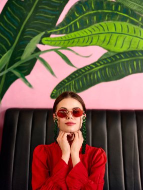 Şık bir kadın, içi palmiye ağaçları ve tropikal titreşimlerle dolu canlı bir kanepede uzanır..