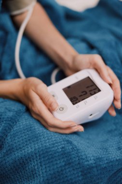 Yatakta, mavi battaniyenin altında elektronik tansiyon monitörüyle yatan kişi..