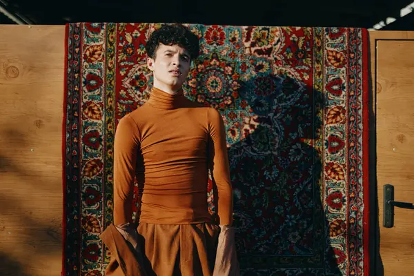 stock image A young model wearing a brown turtleneck stands poised in front of a colorful patterned rug The interplay of light and shadow adds depth to the scene