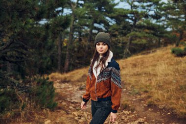 Şık bir şapkası ve ceketi olan genç bir kadın ormanda huzurlu bir yürüyüş yapar. Doğayı ve sükuneti kucaklar.