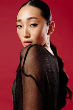 Uzun saçlı, siyah bluzlu, kırmızı arka planda poz veren, elleri kalçasında, yana bakan Asyalı bir kadın. moda konsepti.