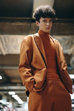 Modern, endüstriyel ve yumuşak ışıklandırmalı tek renkli turuncu kıyafetler giyen şık bir genç adam.