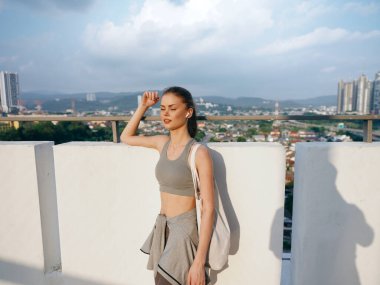 A young woman stands confidently on a rooftop, looking off into the distance, with a modern city in the background clipart