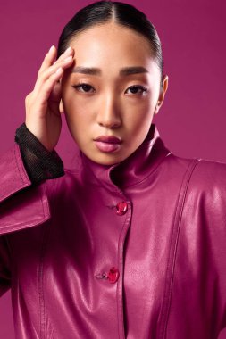 Mor deri ceketli ve siyah gömlekli Asyalı bir kadın mor arka planda elleri kafasında poz veriyor. şık esmer model..